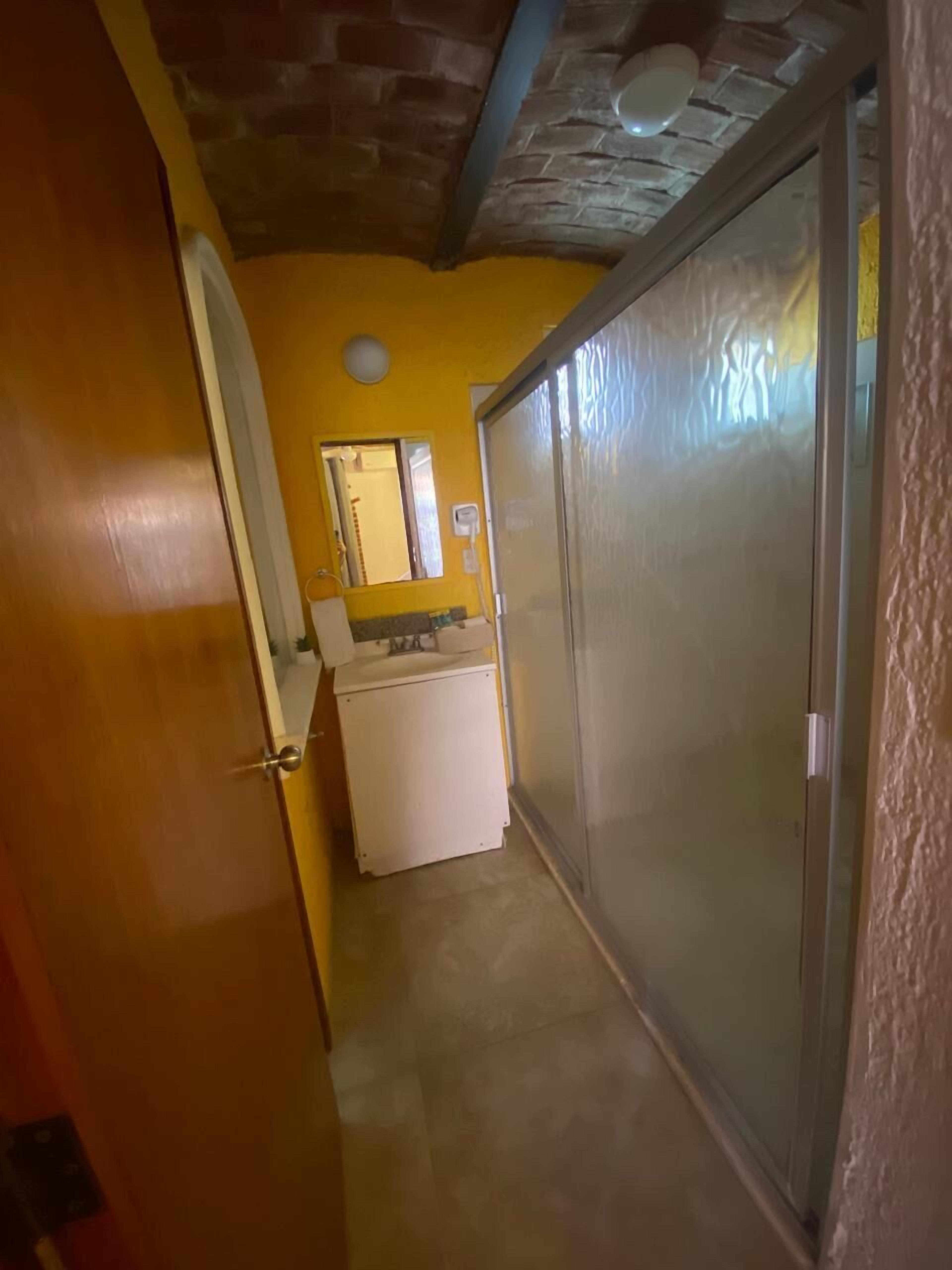 A narrow hallway with a white refrigerator, a mirror, and a door leading to a room.