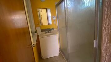 A narrow hallway with a white refrigerator, a mirror, and a door leading to a room.