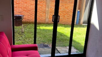 Une pièce avec un canapé rouge, un sol à motifs et une porte-fenêtre coulissante qui donne sur un mur de briques et une cour verdoyante.