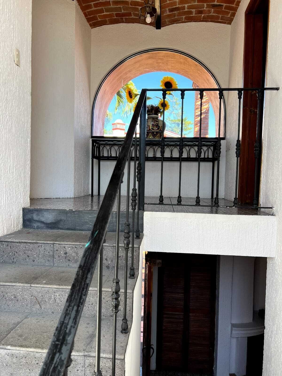 Een trap met een smeedijzeren leuning die leidt naar een balkon met uitzicht op een muurschildering van zonnebloemen en een gebouw.