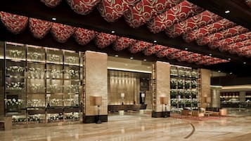 Un hall d’entrée spacieux, doté d’un sol en marbre poli, d’un grand plafond orné de motifs rouges et de vitrines en verre remplies de fleurs blanches.