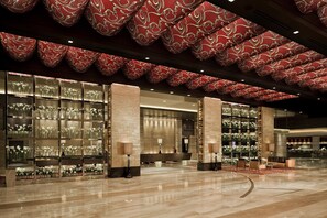 A spacious lobby with a polished marble floor, large red patterned ceiling, and glass display cases filled with white flowers.