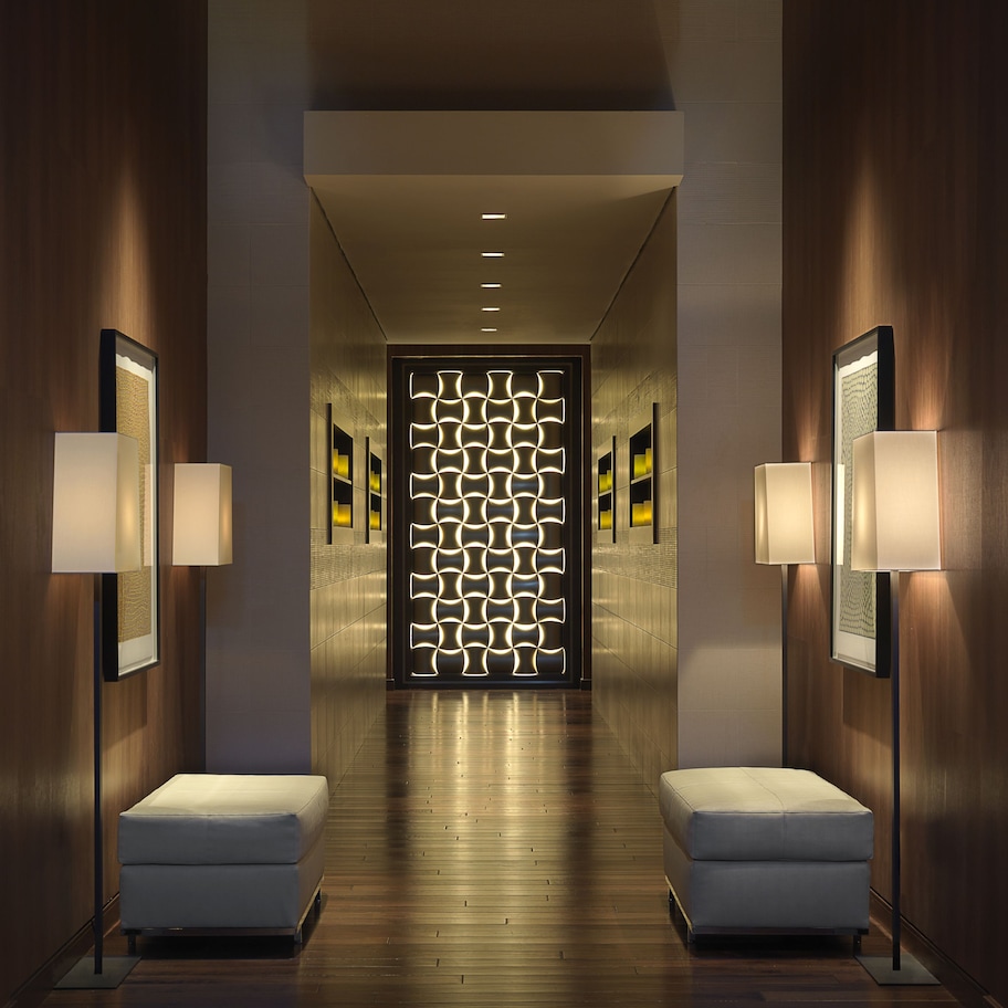 A modern hallway with wooden flooring, recessed lighting, and two seating areas with cushioned benches.