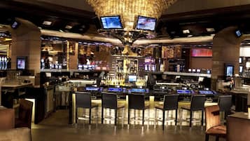 Zona de bar con una gran lámpara circular, varios mostradores y diferentes disposiciones de asientos.