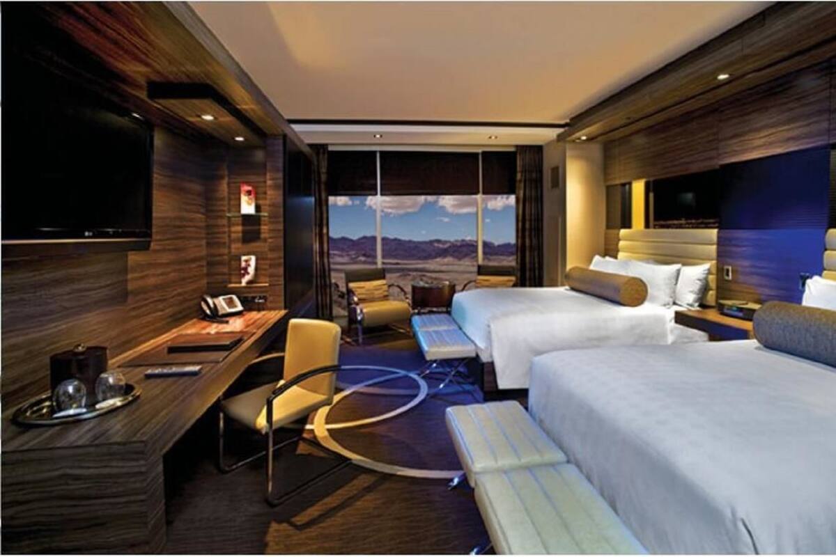 Een hotelkamer met een groot bed, een bureau met een computer, een stoel en een aan de muur bevestigde televisie.