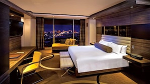 Une chambre d’hôtel moderne, dotée d’un grand lit, d’un bureau, d’une chaise et offrant une vue sur la ville la nuit.