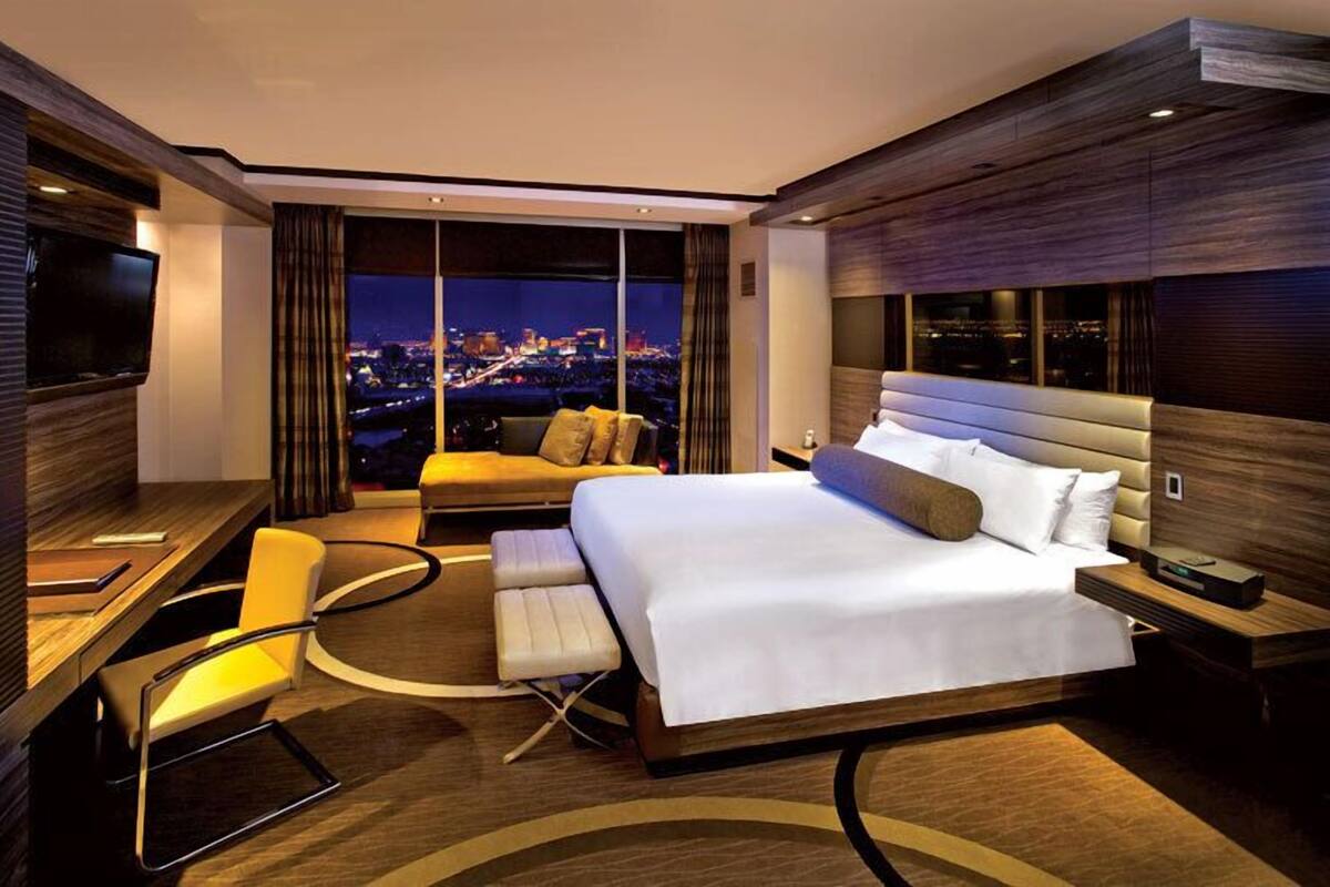 Een moderne hotelkamer met een groot bed, een bureau, een stoel en uitzicht op de stad 's nachts.