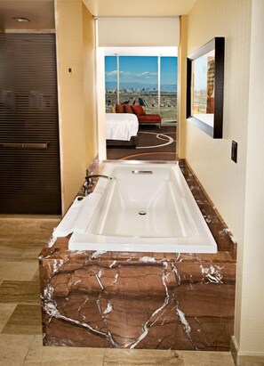 A modern bathroom with a large bathtub, marble countertop, and a view of a cityscape through a large window.