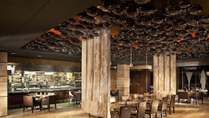 Un restaurant moderne doté d’une longue table à manger, de hauts piliers en bois et d’un plafond orné de décorations sphériques réfléchissantes.