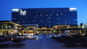 Un hôtel avec un grand logo en forme de « M », des piscines extérieures et des espaces aménagés pour se détendre.