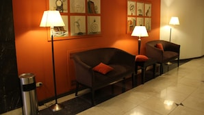 A hotel lobby with a brown sofa, a chair, a trash can, and two floor lamps. - Ayacucho Palace Hotel (Buenos Aires)