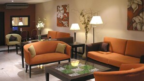 A modern living room with orange sofas, a glass coffee table, and a TV in the background. - Ayacucho Palace Hotel (Buenos Aires)