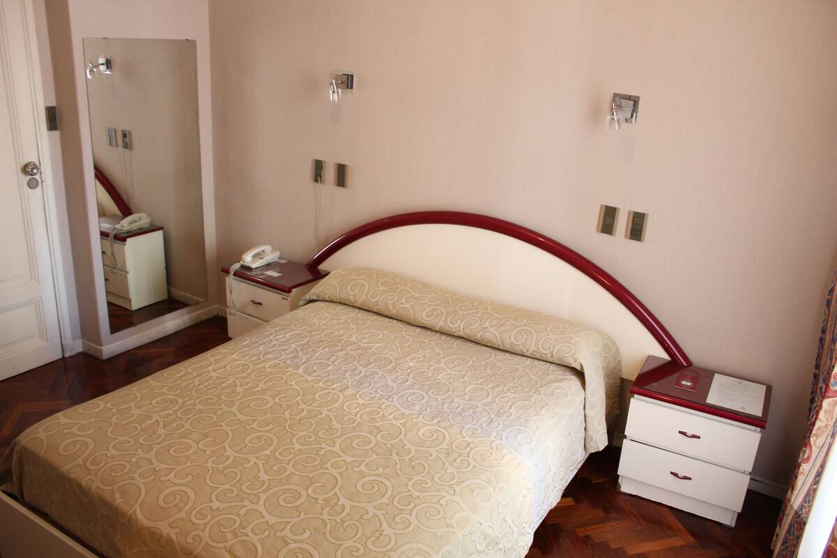 Un dormitorio con cama, mesita de noche, espejo y teléfono.