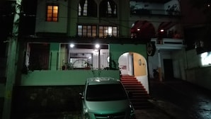 Il s’agit d’un immeuble à deux étages, avec une voiture garée devant. Un escalier mène à l’entrée, et l’immeuble possède de nombreuses fenêtres.