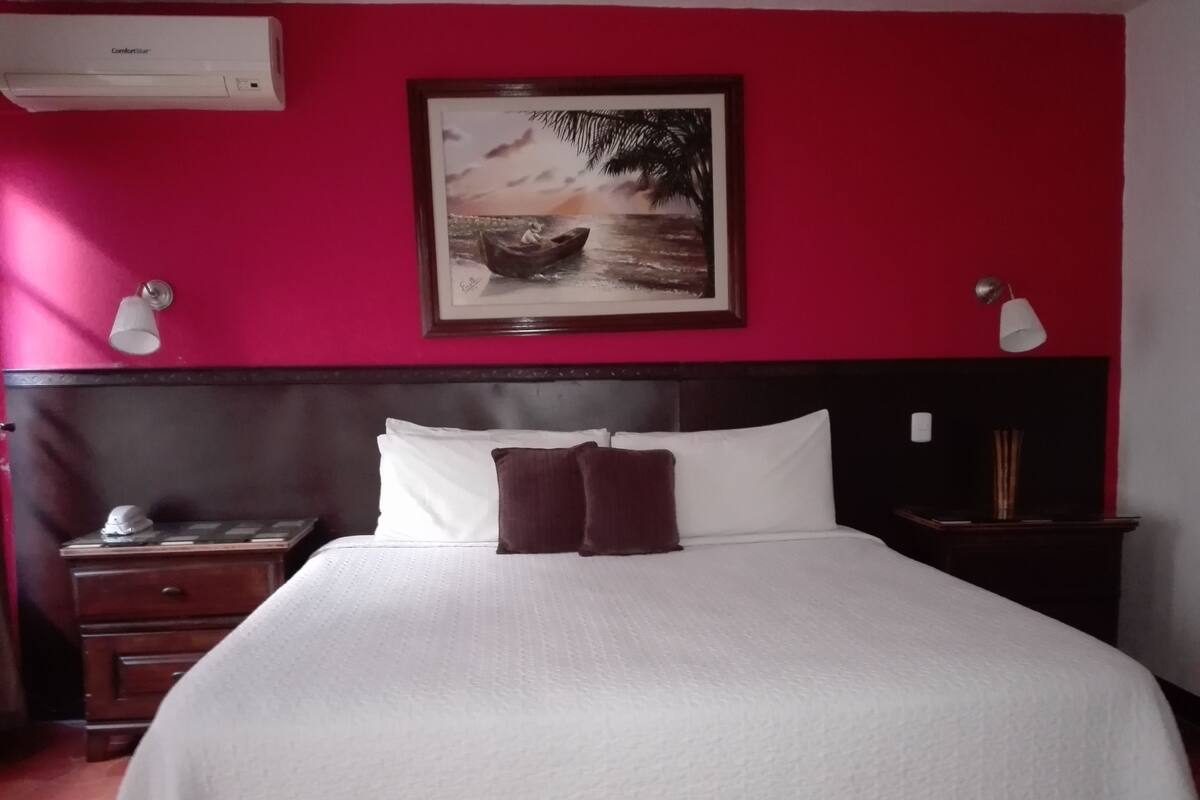 Une chambre d’hôtel avec un grand lit, une table de chevet, un bureau et un tableau encadré au mur.