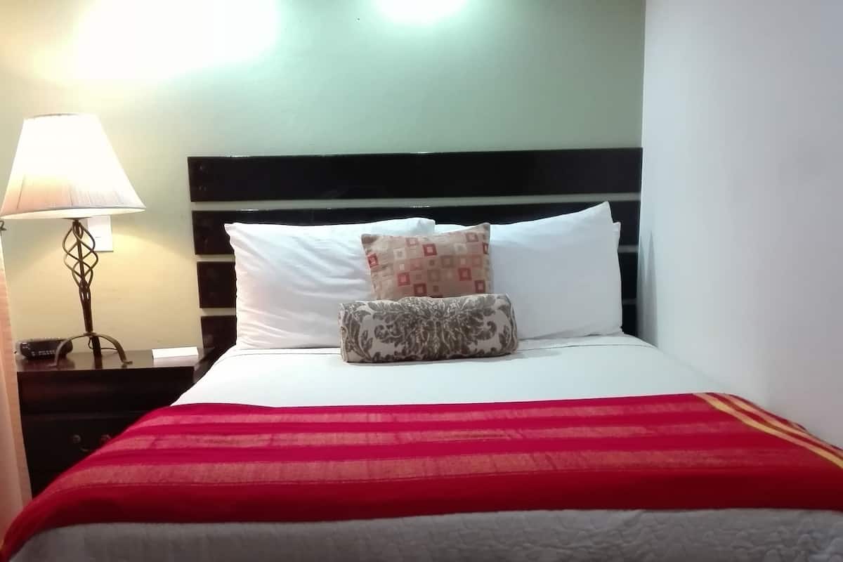 Un lit bien fait, avec une couvre-lit rouge et blanche, deux oreillers et une lampe de chevet.