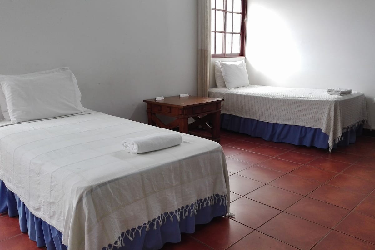 Une chambre d’hôtel avec deux lits, une table de chevet en bois et une fenêtre avec des rideaux.