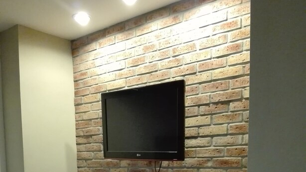 Une pièce avec un mur en briques, un téléviseur fixé au mur et un banc agrémenté d’objets décoratifs.