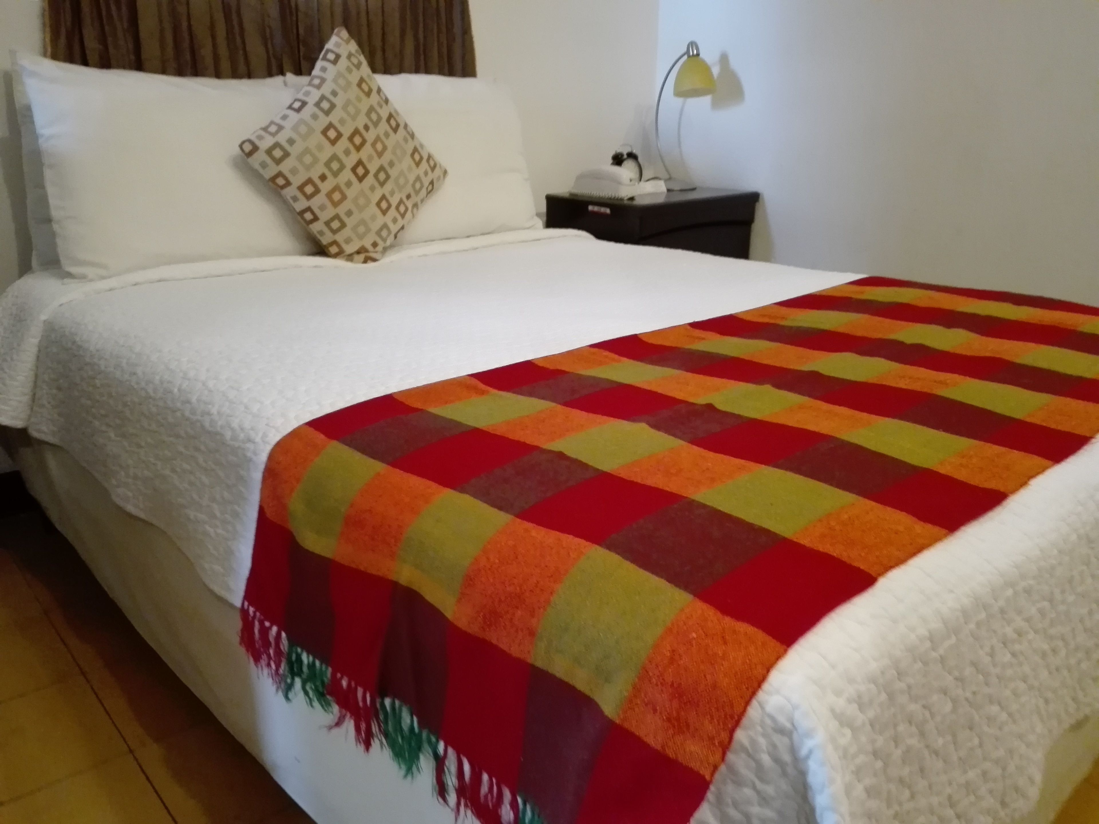 A neatly made bed with a white comforter and a colorful checkered blanket.