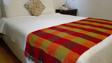 A neatly made bed with a white comforter and a colorful checkered blanket.
