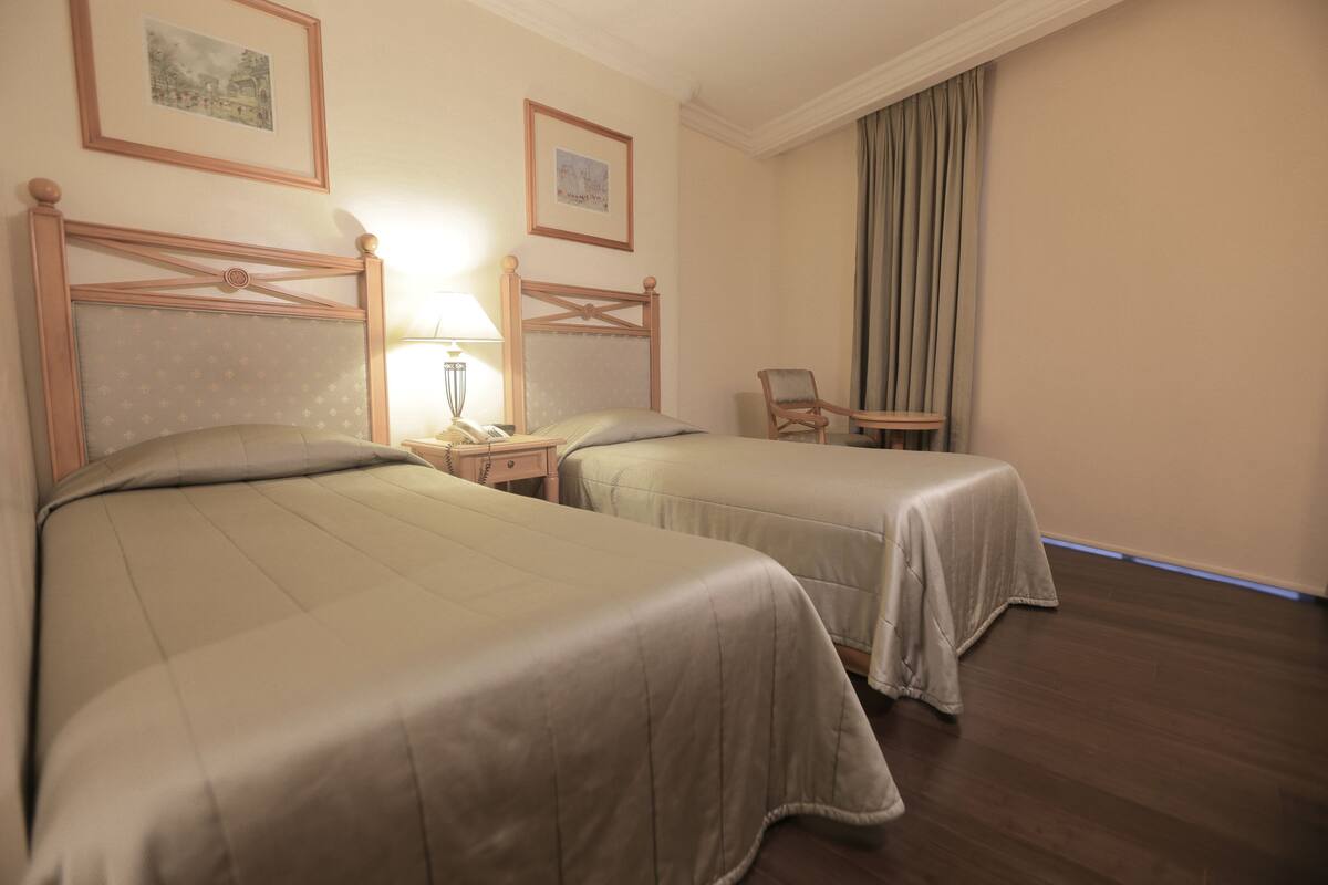 A hotel room with two beds, a nightstand, a chair, and a window with curtains.