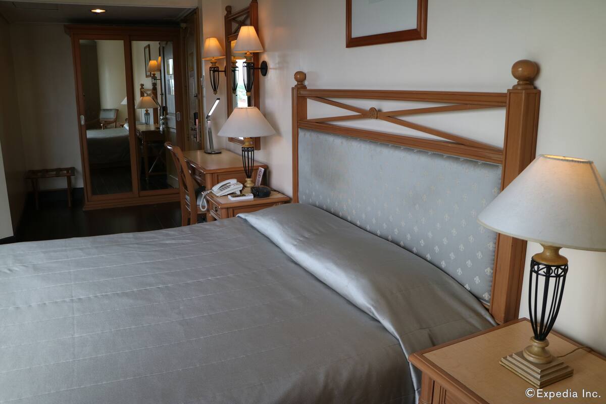 A hotel room with a bed, bedside lamps, a desk with a telephone, and a mirror.