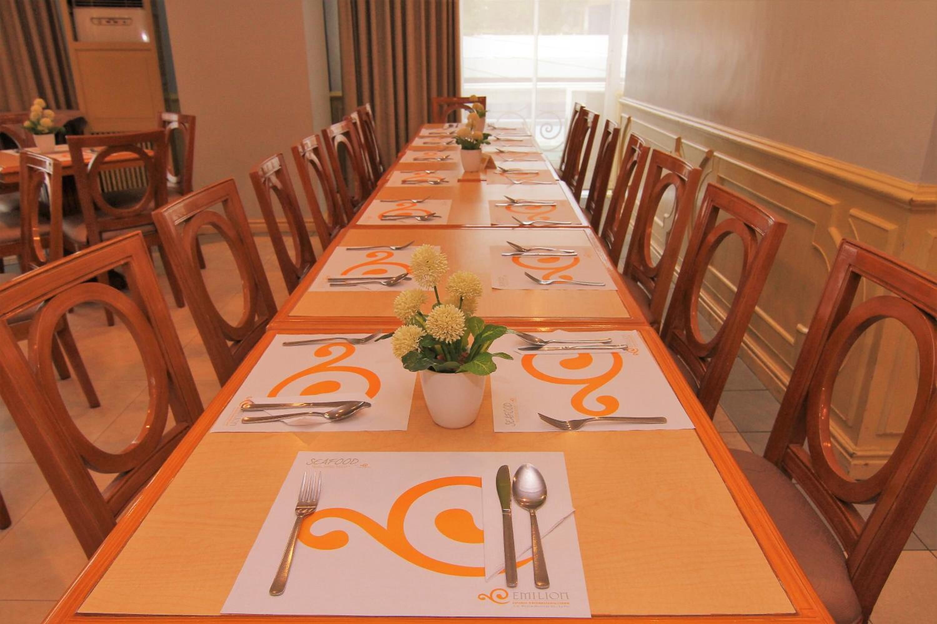 A long dining table with chairs, set for a meal with place settings and a floral centerpiece.