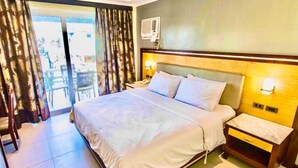 A hotel room with a large bed, a bedside table, a nightstand, and a sliding glass door leading to an outdoor area. - MO2 Westown Hotel Iloilo (Iloilo)