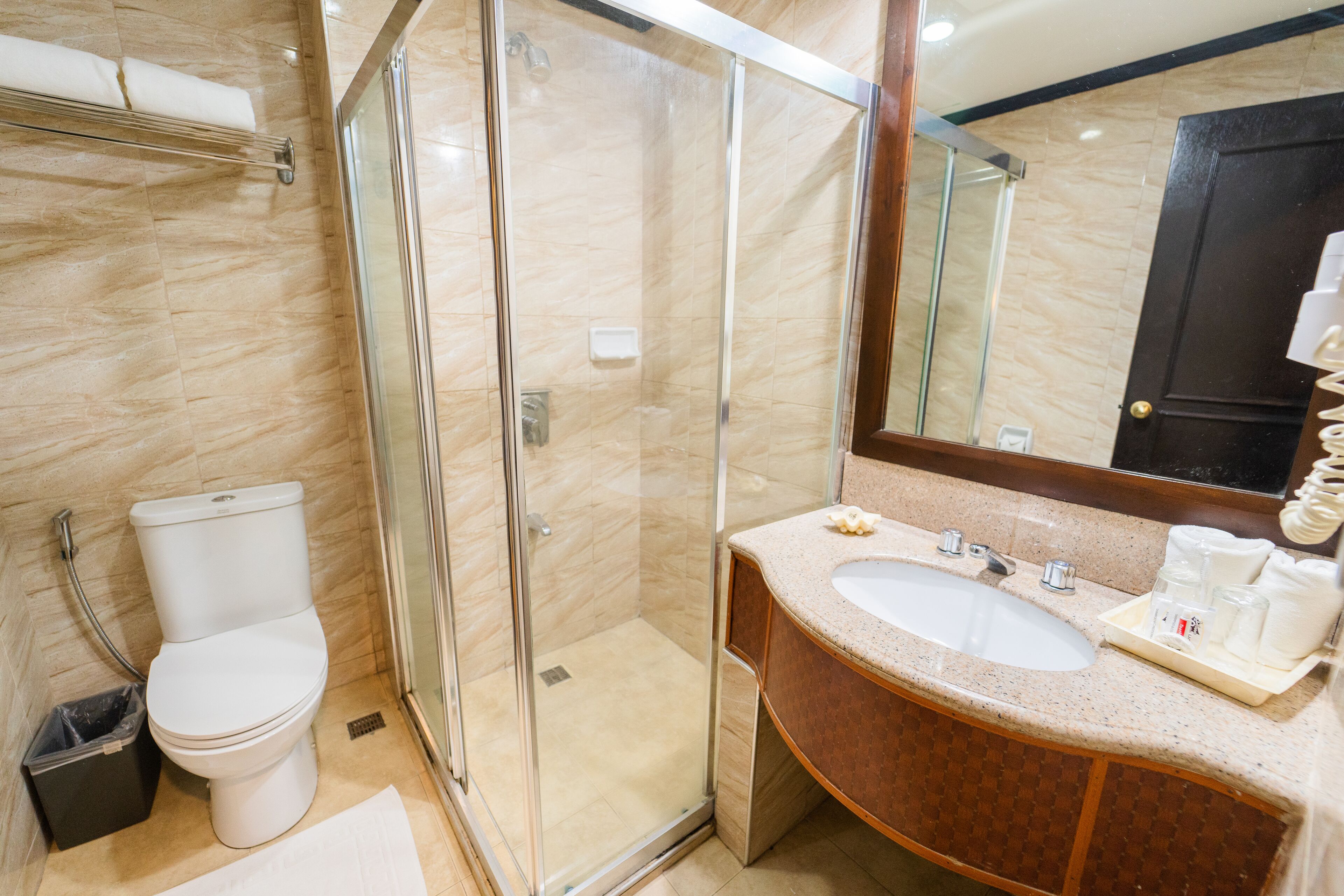 Un baño moderno con ducha de vidrio, inodoro blanco y zona de lavamanos con azulejos de mármol.