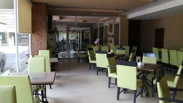 Un restaurant avec des chaises et des tables vertes, un mur orné de motifs et une vue sur la rue.