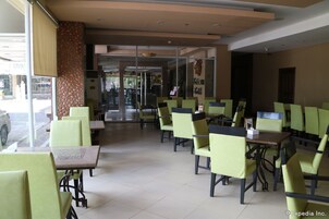 Un restaurante con sillas y mesas verdes, una pared con diseño y vistas a la calle.