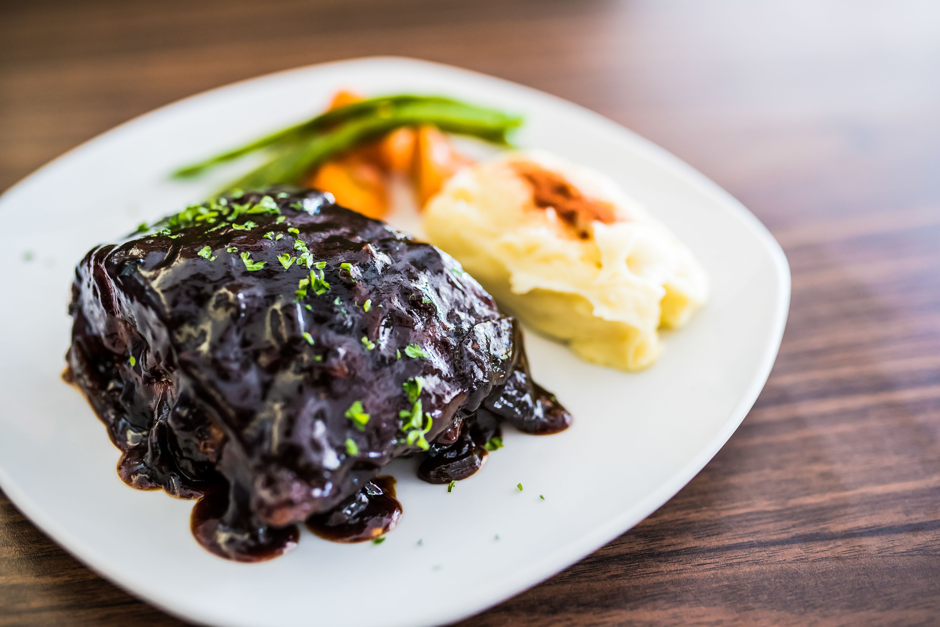 A plate with a dark glazed meat, mashed potatoes, and green vegetables.