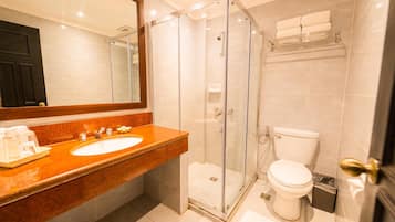 Un baño moderno con ducha envuelta en vidrio, lavamanos blanco y encimera de mármol, y un inodoro.