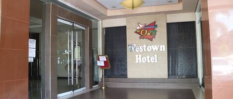 La entrada del Hotel Westown, con puerta de vidrio, mostrador de recepción y un cartel.