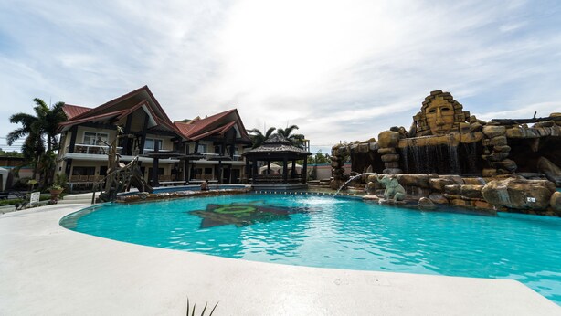 A swimming pool with a waterfall feature, a gazebo, and a large house with a red roof. - MO2 Westown Hotel Iloilo (Iloilo)