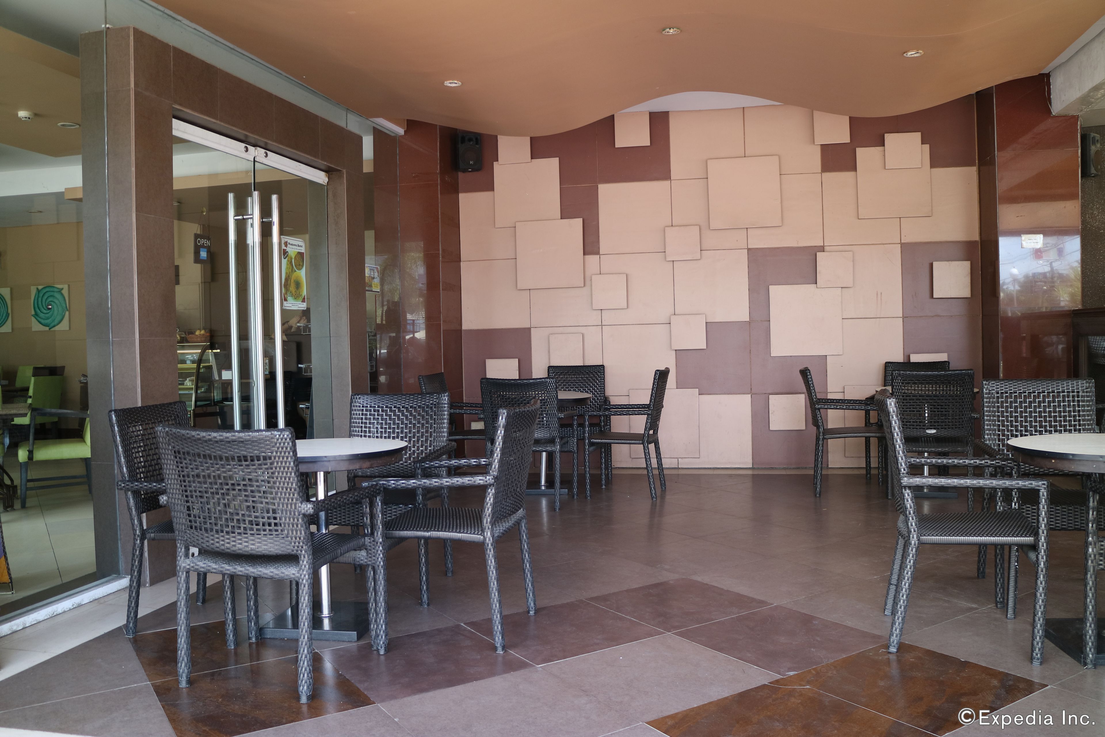 A restaurant with wicker chairs and tables, a tiled floor, and a wall with geometric patterns.