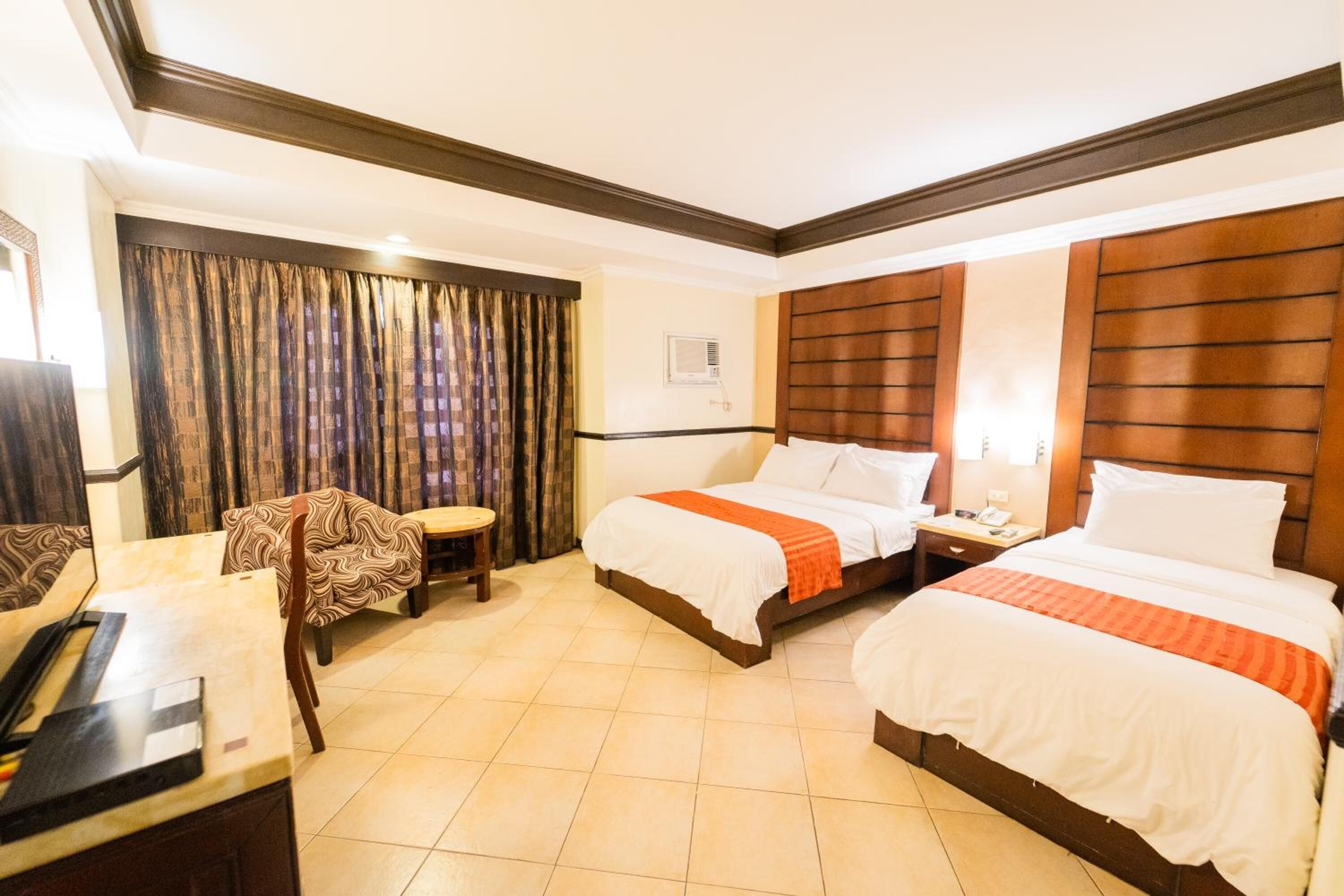 A hotel room with two beds, a desk, a chair, and a curtain.