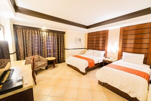 A hotel room with two beds, a desk, a chair, and a curtain.