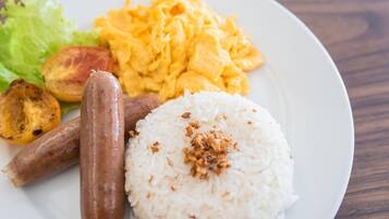 A plate with white rice topped with fried onions, two grilled sausages, scrambled eggs, and a side of lettuce and roasted tomatoes.
