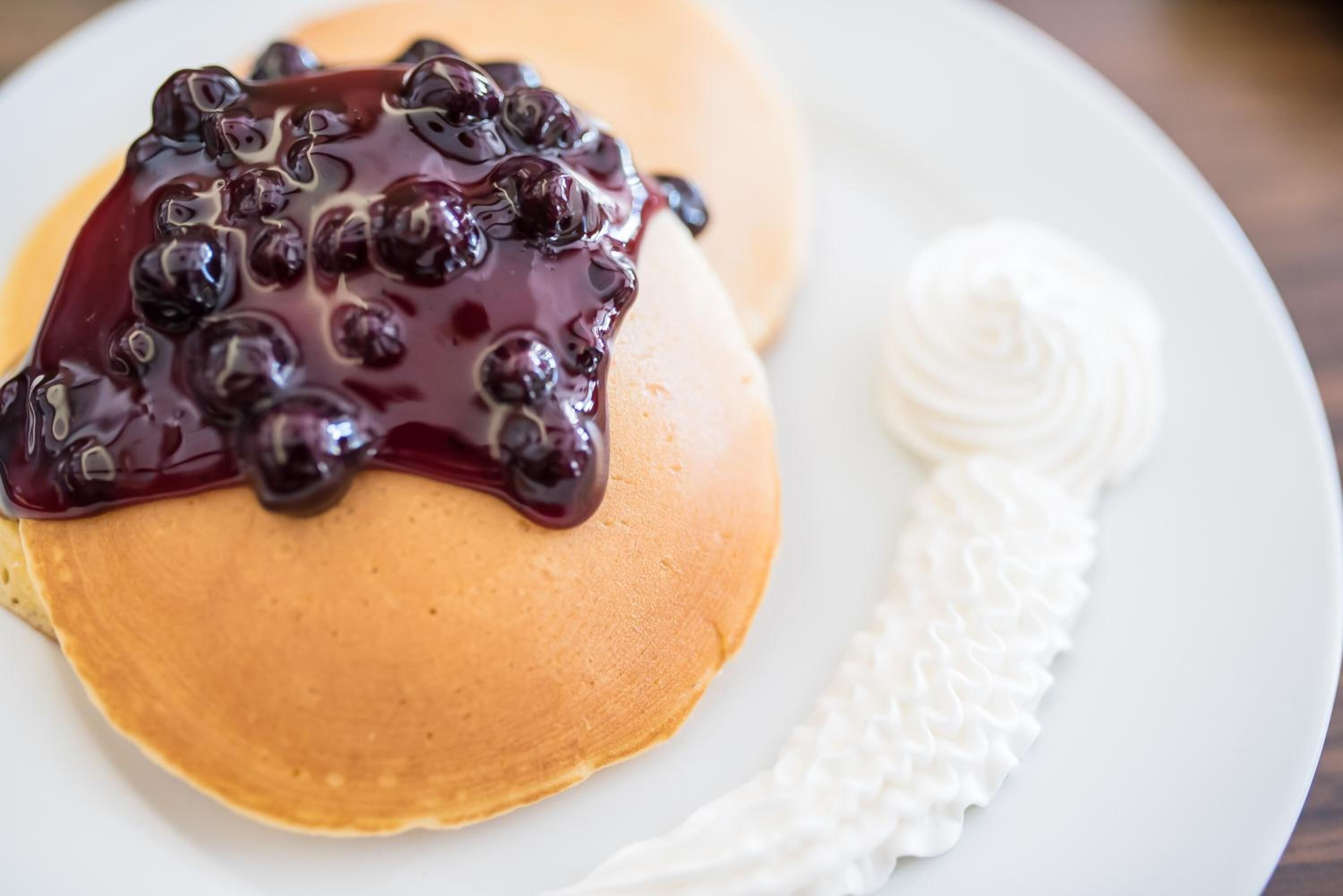 A plate with pancakes topped with blueberry compote and a dollop of whipped cream.