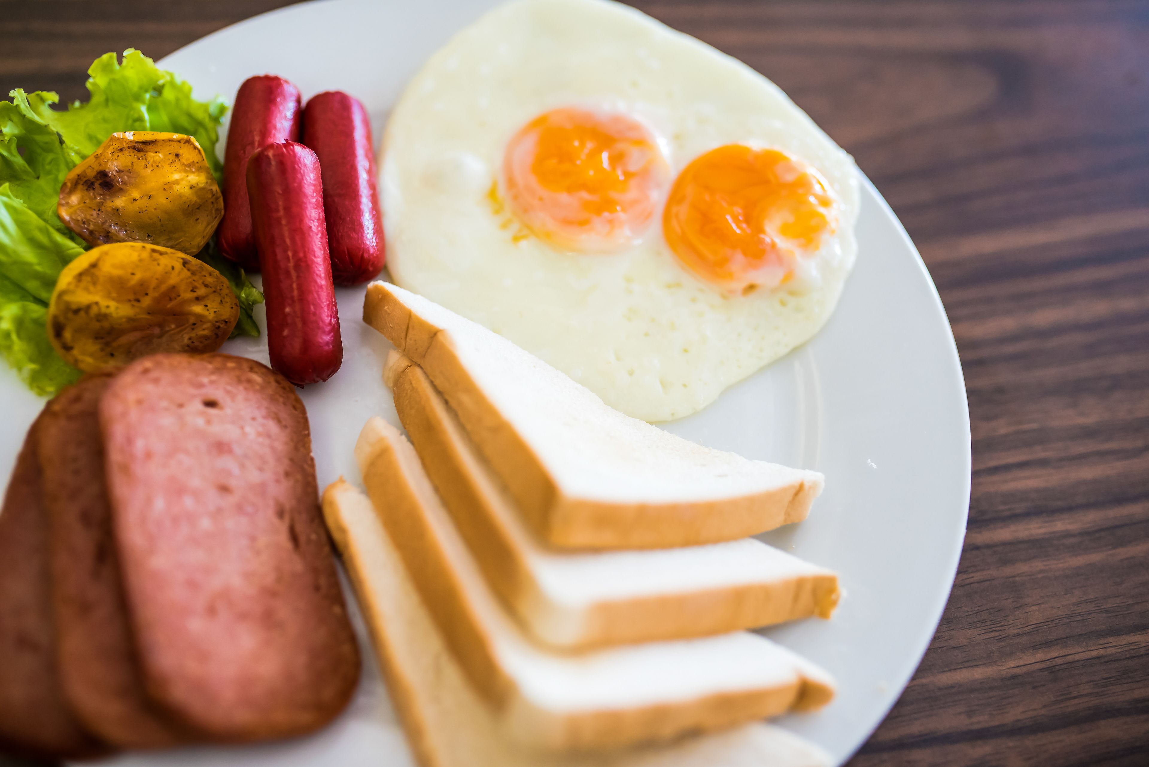 A plate with a fried egg, sausages, roasted potatoes, and slices of white bread.