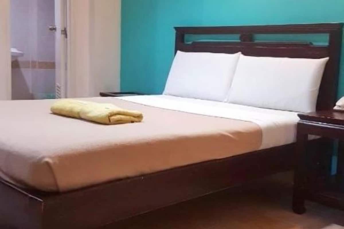 A neatly made bed with white linens and a yellow towel, a wooden headboard, and a nightstand with a lamp.