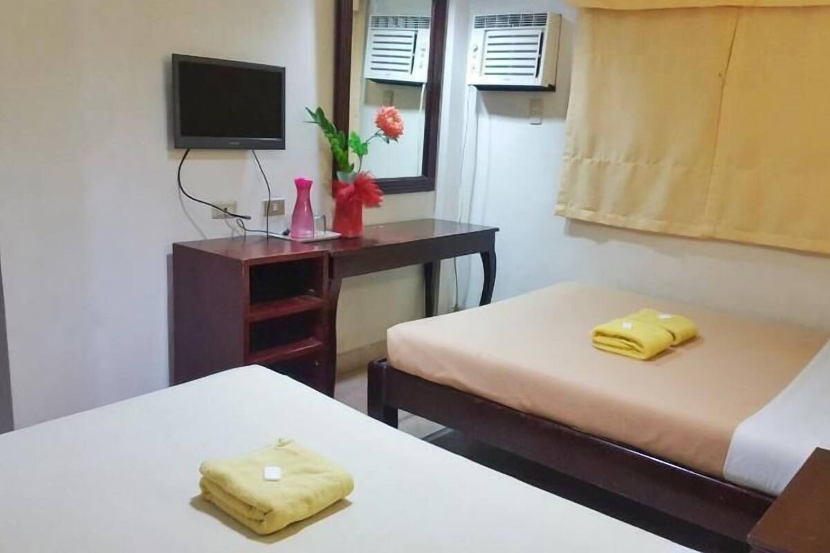 A hotel room with two beds, a desk, a TV, and air conditioning units.