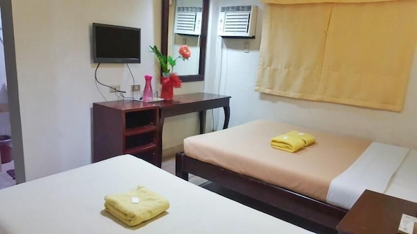 A hotel room with two beds, a desk, a TV, and air conditioning units.