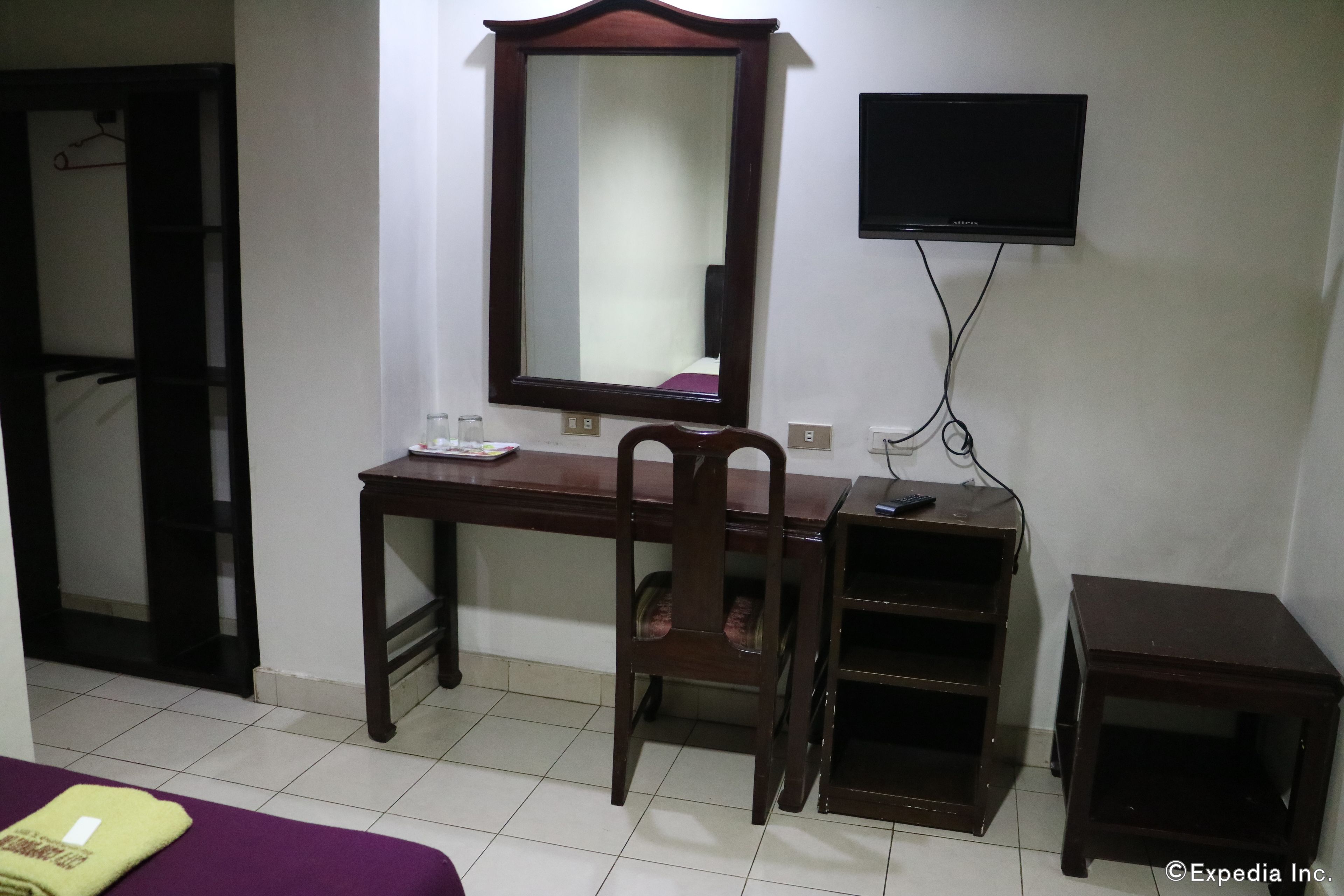 A hotel room with a wooden desk, a chair, a television, and a small table.