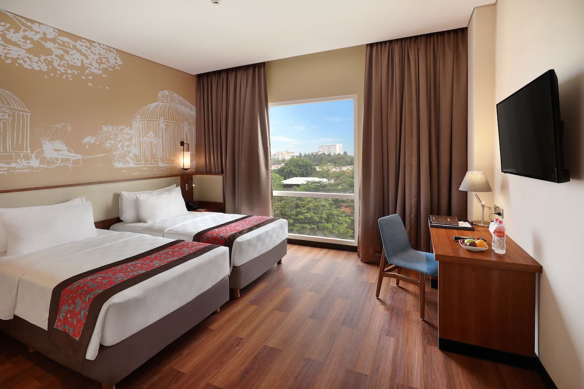 Une chambre d’hôtel avec deux lits, un bureau avec une chaise, une télévision et une grande fenêtre avec des rideaux.