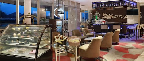 Un hall d’hôtel doté d’une vitrine où sont exposés des desserts, de sièges confortables, d’un bar et d’une vue sur les montagnes.