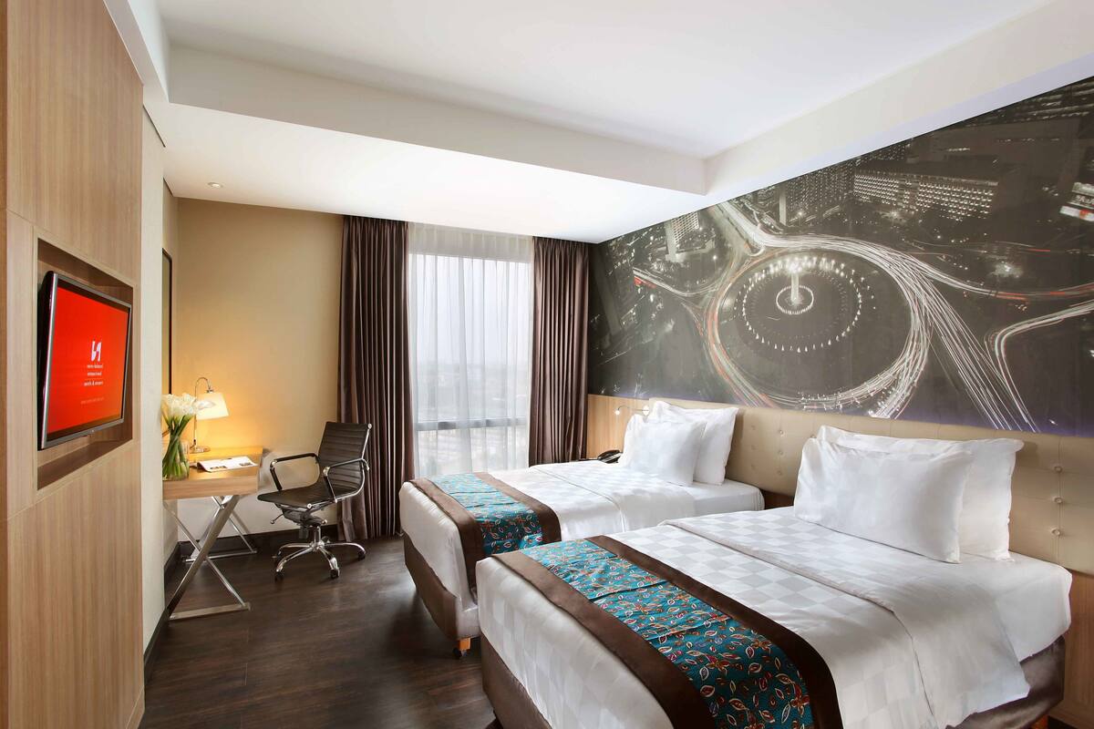 Une chambre d’hôtel avec deux lits, un bureau avec une chaise, une télévision et une grande fenêtre avec des rideaux.