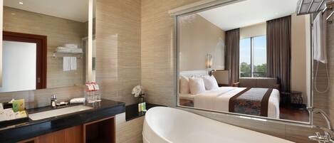 A modern hotel bathroom with a large bathtub, a vanity with a mirror, and a large mirror reflecting the room.