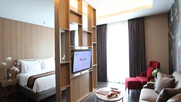 Habitación de hotel con cama, televisor, sillón rojo, sofá y una mesita con frutas.